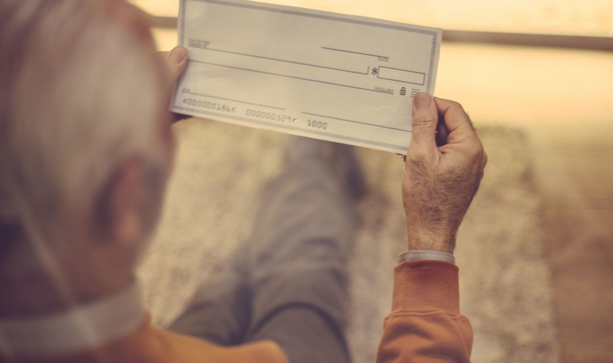 Days of age are insured. Senior man holding bank check. Close up. Focus on hand.