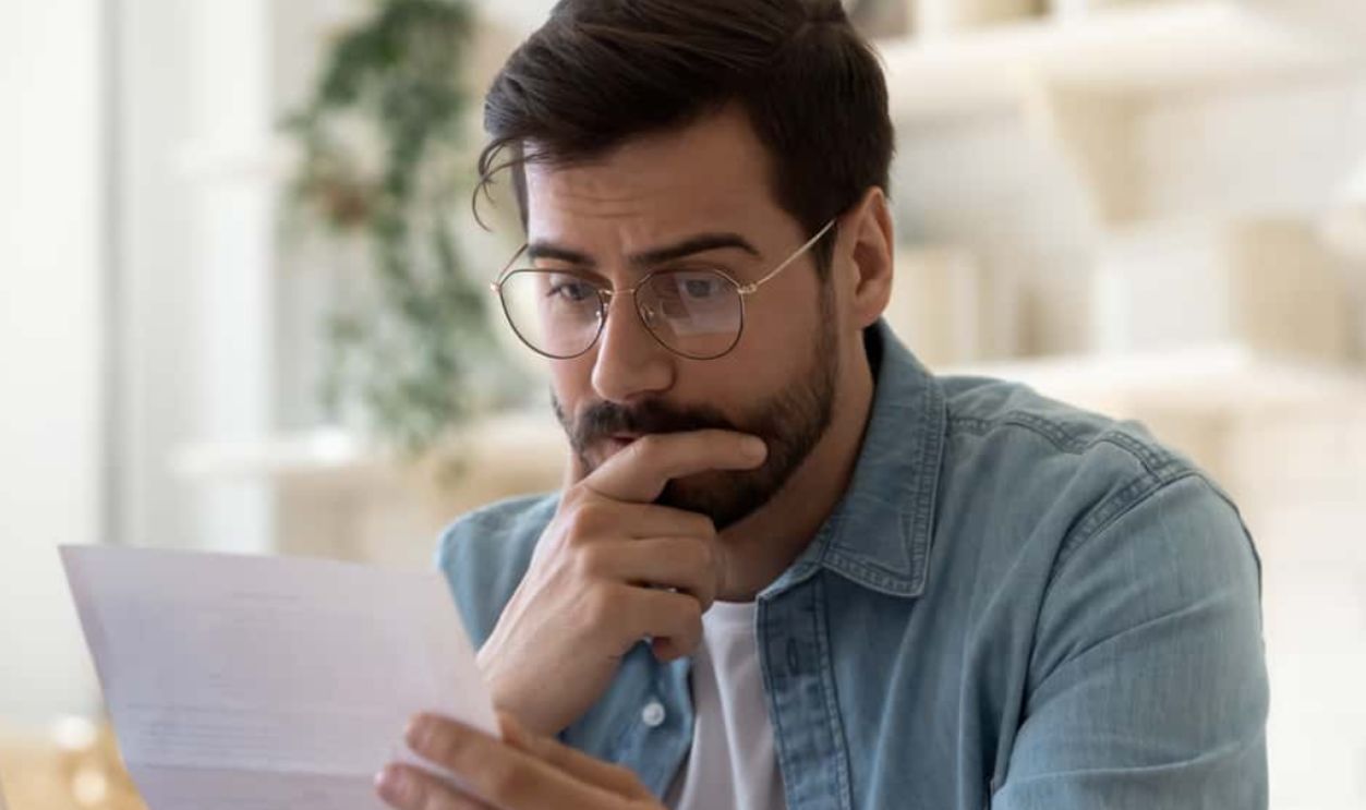 Frustrated millennial guy in glasses read bad unpleasant news in postal letter, sad confused young man consider paperwork get negative answer in post correspondence, eviction or dismissal notice