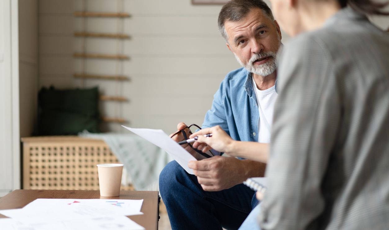 Middle aged senior old couple holding documents reading paper bills paying bank loan online, calculating pension fees, payments, taxes, planning family retirement money finances at home.