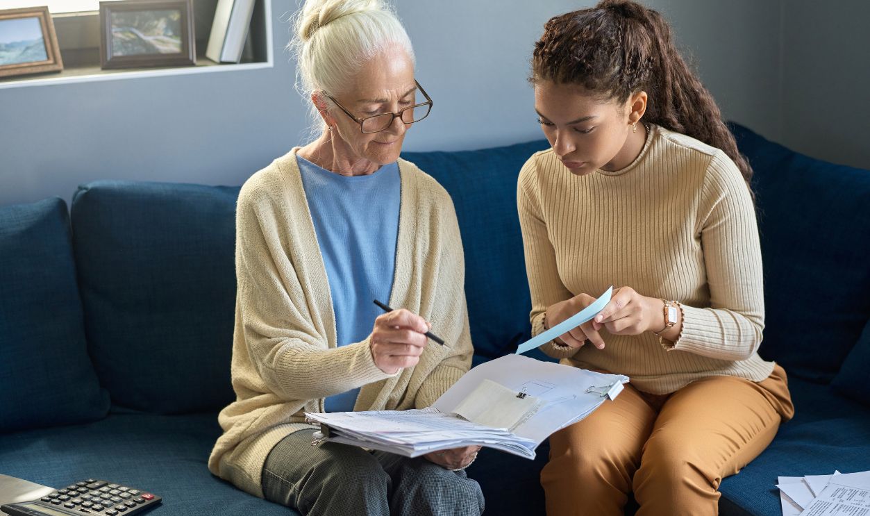 Youthful girl with small paper and her grandmother looking at document