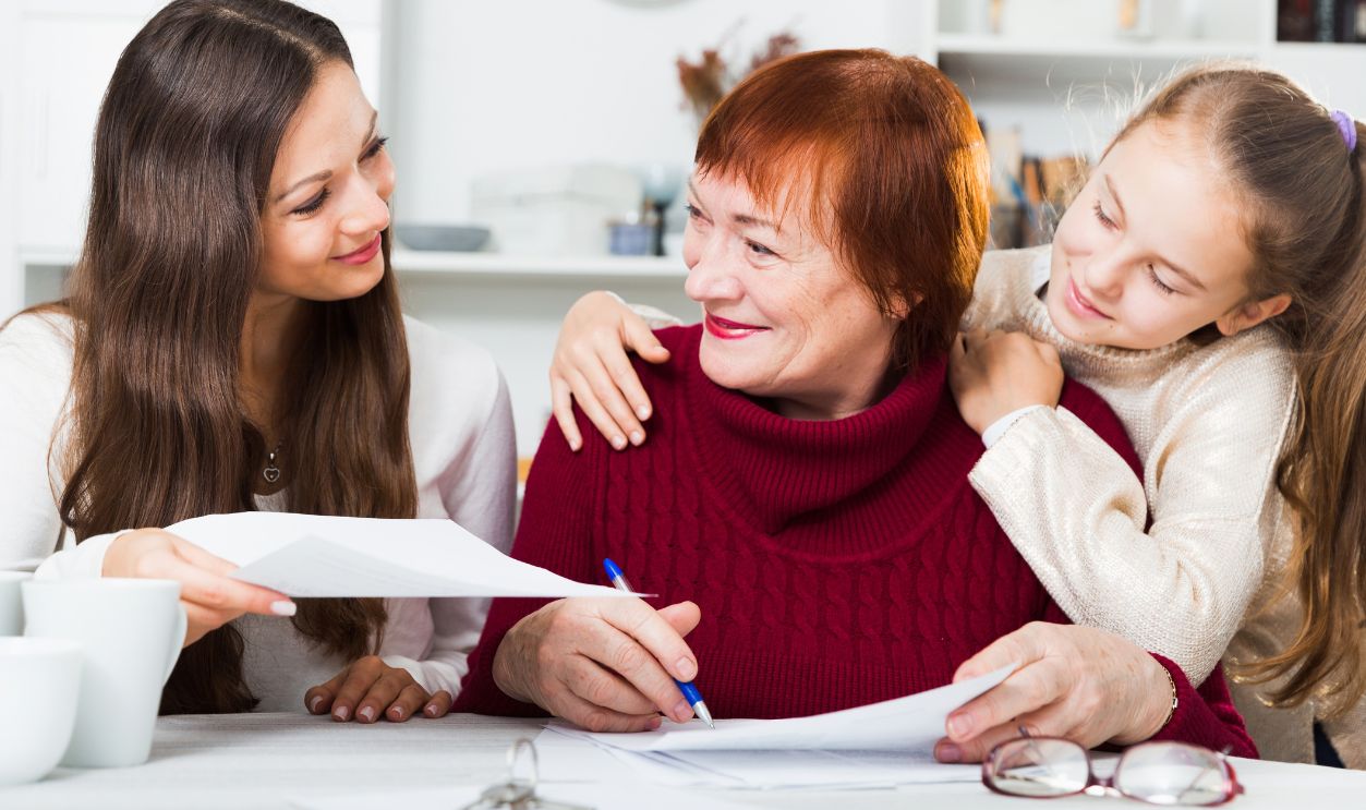 Smiling senior woman with daughter and granddaughter writing papers at home