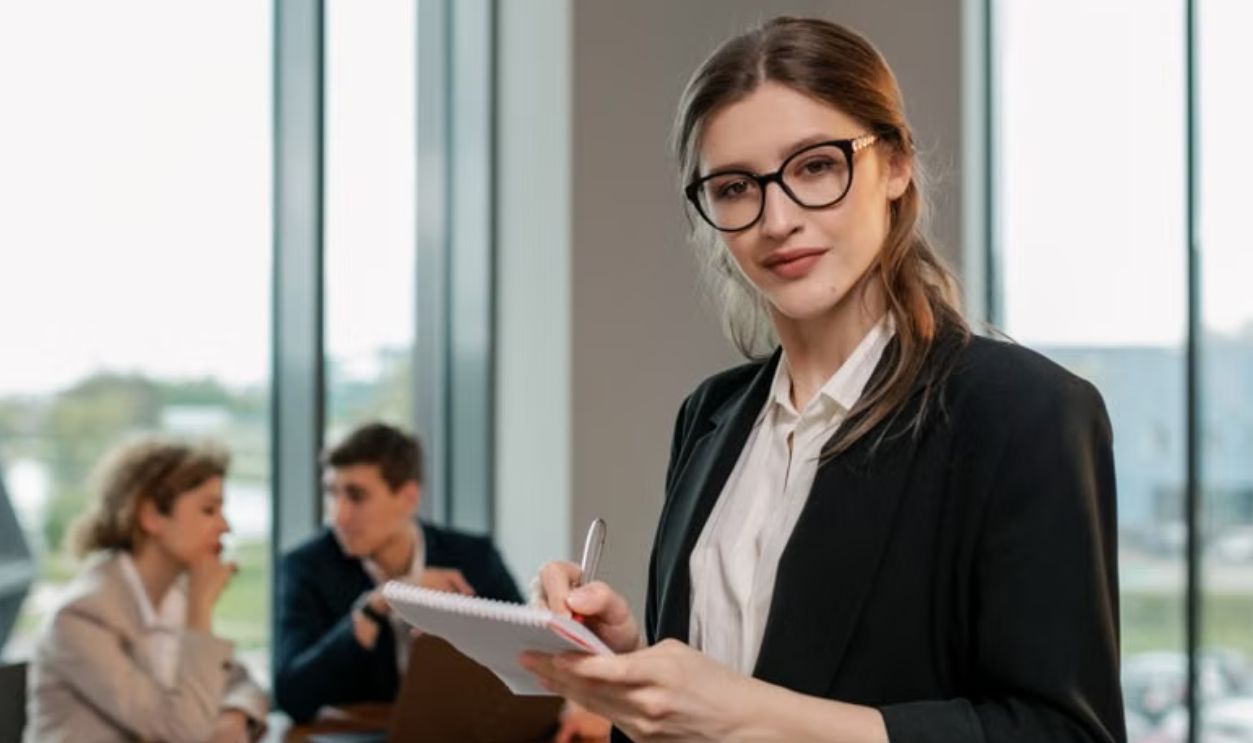 Confident businesswoman holding notebook during meeting in modern office setting.