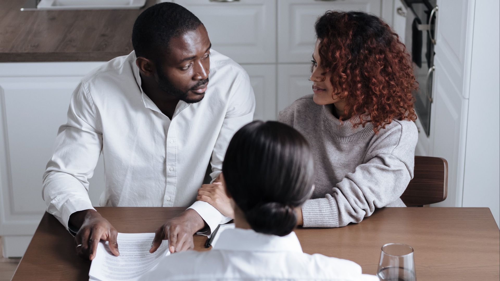 Three adults discussing documents at a table in a modern kitchen.