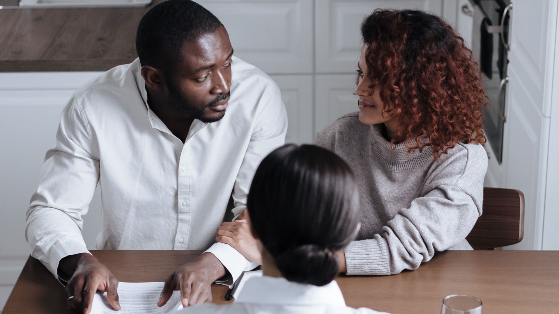 Three adults discussing documents at a table in a modern kitchen.