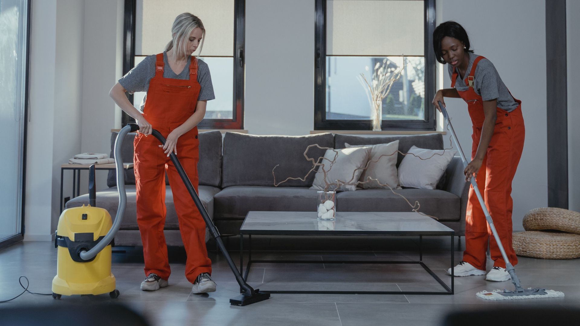 Two professional cleaners working in a living room with modern decor.