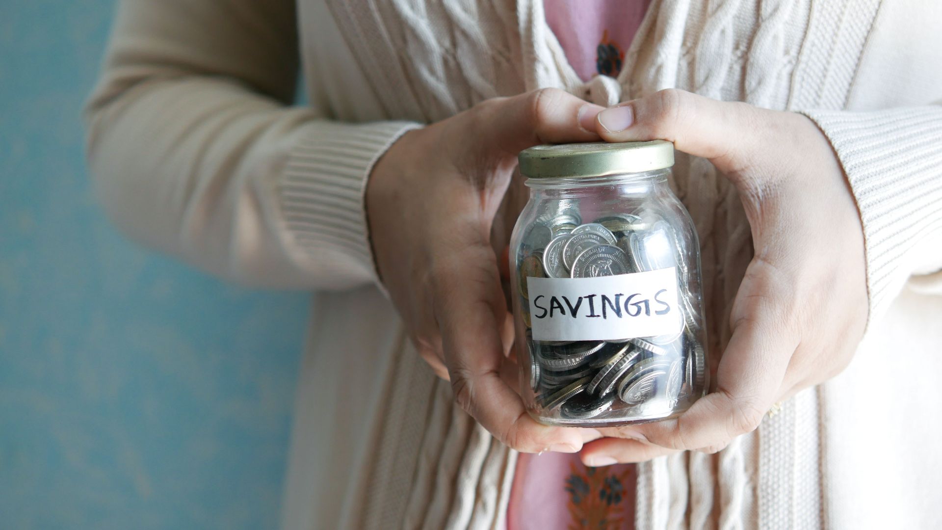Woman holding a jar labeled 'savings' filled with coins, representing financial savings.