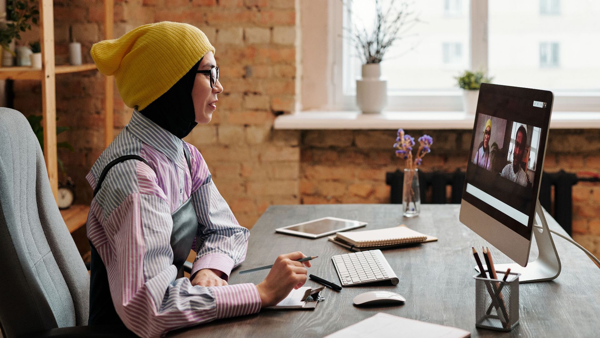 Businesswoman wearing casual attire participates in a video conference in a modern office setting.