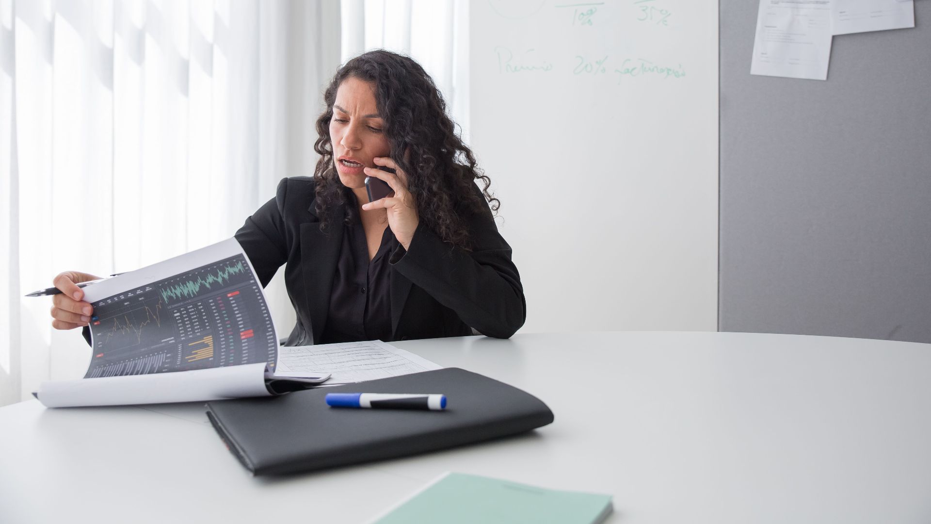 Focused businesswoman reviewing data charts during a phone call in a modern office setting.