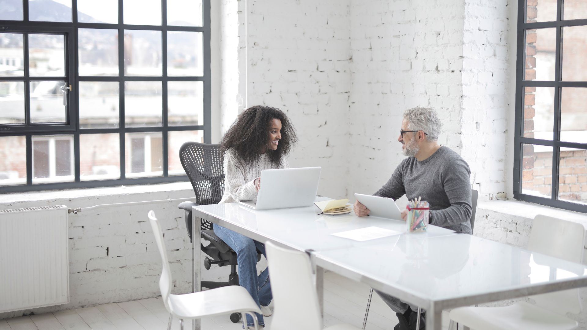 Two professionals collaborating in a bright, modern office space with laptops.