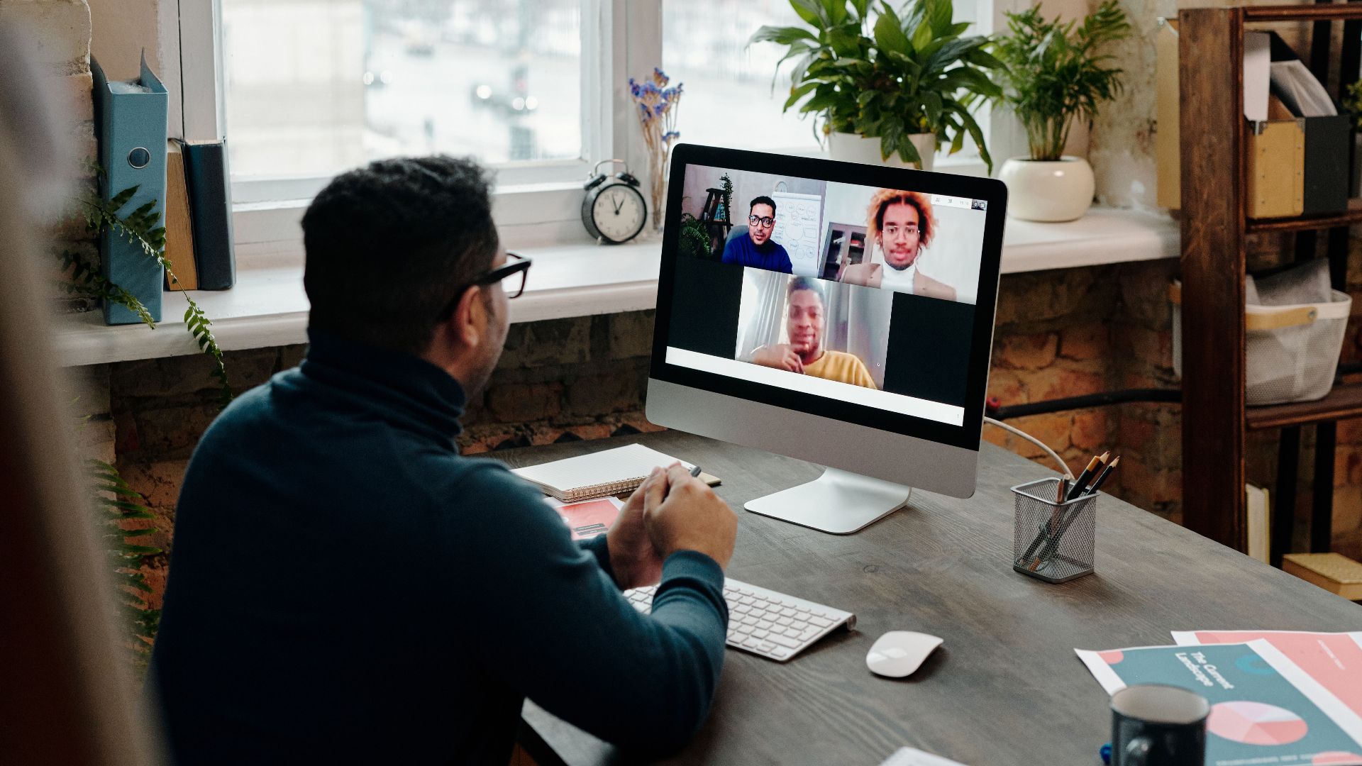 Man participating in video call at desktop computer in stylish office setting with greenery.