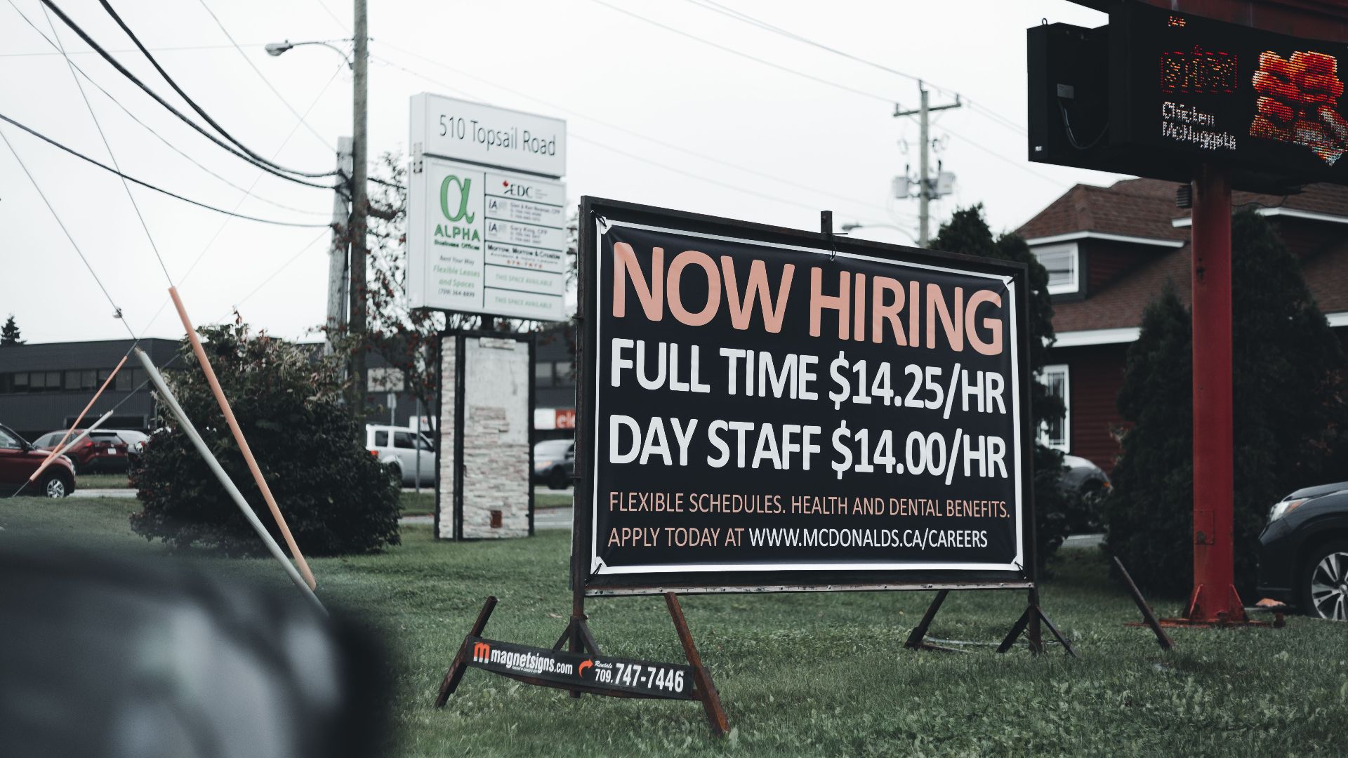 Outdoor hiring sign advertising restaurant job openings with competitive wages and benefits.