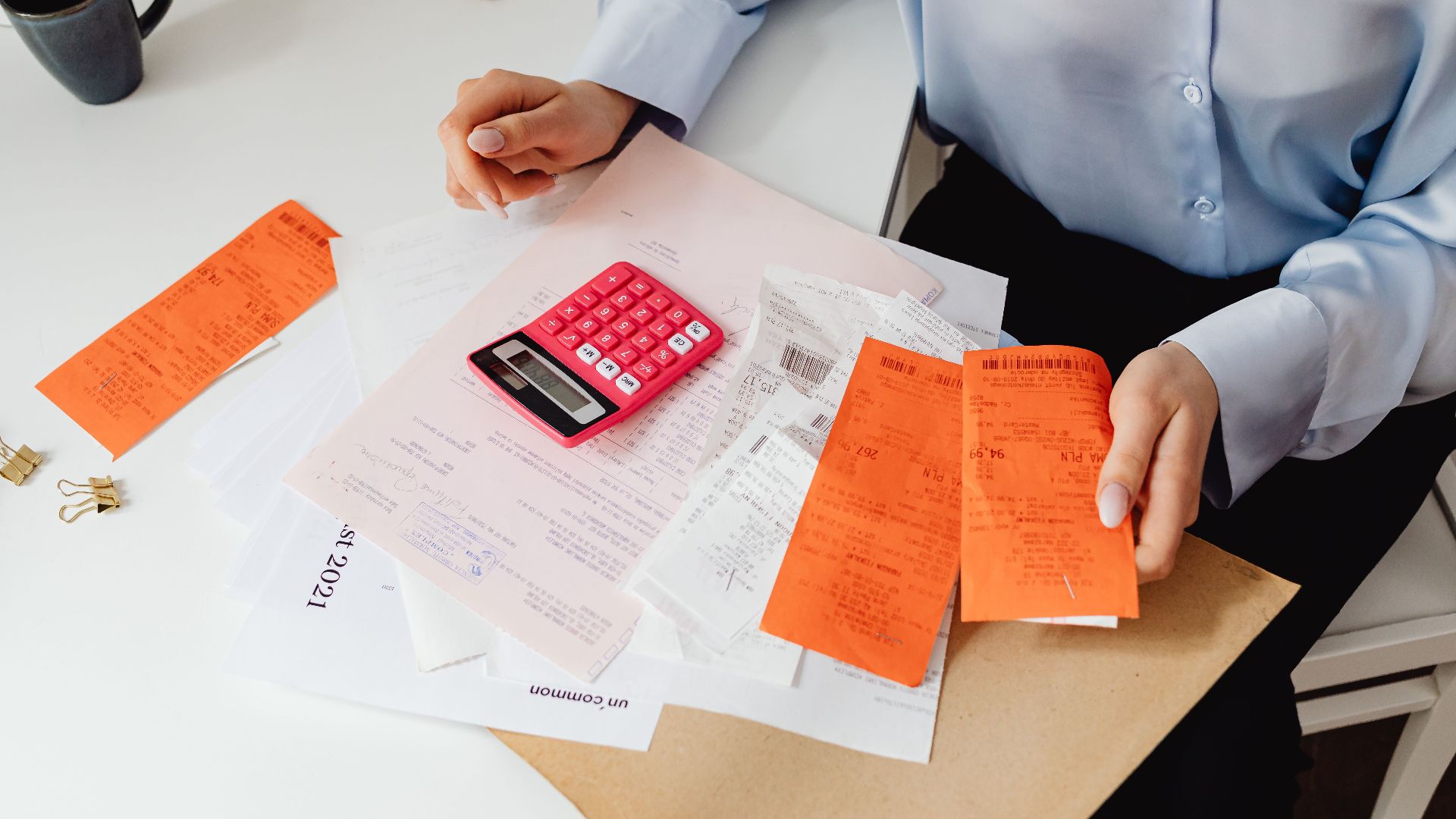 A woman reviews receipts and calculates expenses at a desk with a pink calculator.