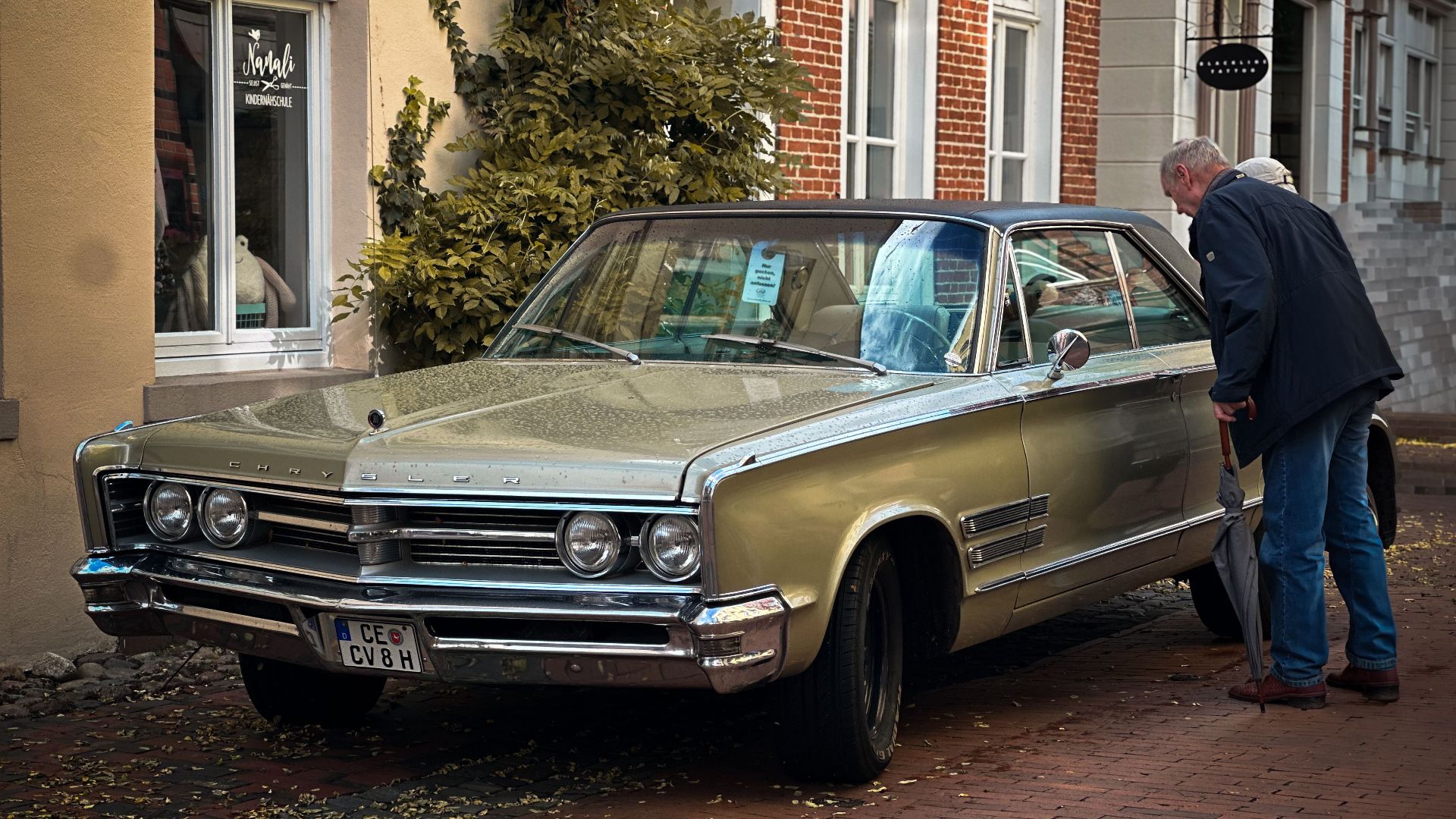 Classic Chrysler parked on a cobbled street in Leer, Germany, with onlookers admiring its vintage charm.