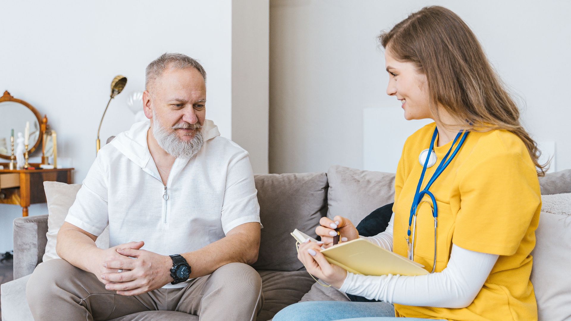 A healthcare professional smiles while consulting with an elderly man in a cozy indoor setting.