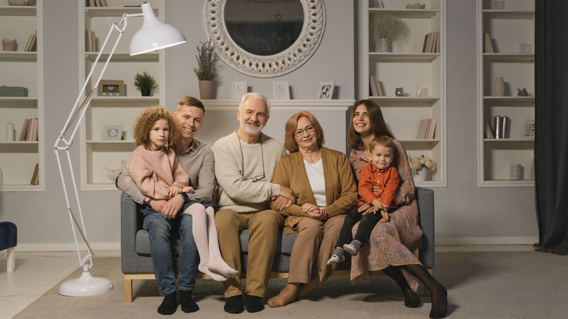 A multi-generational family sitting together on a sofa in a warm living room.