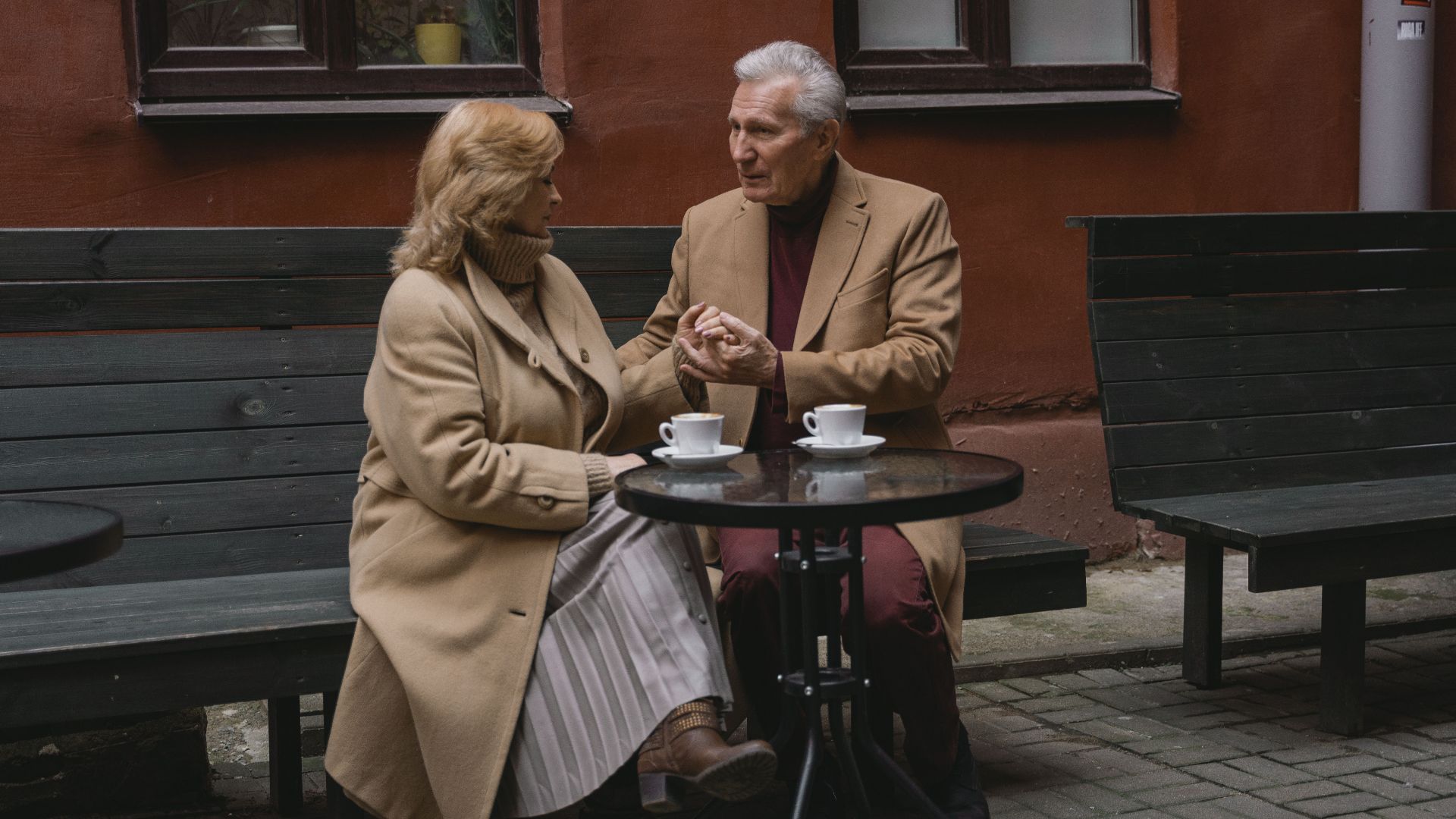 An elderly couple enjoys a conversation over coffee at an outdoor cafe.