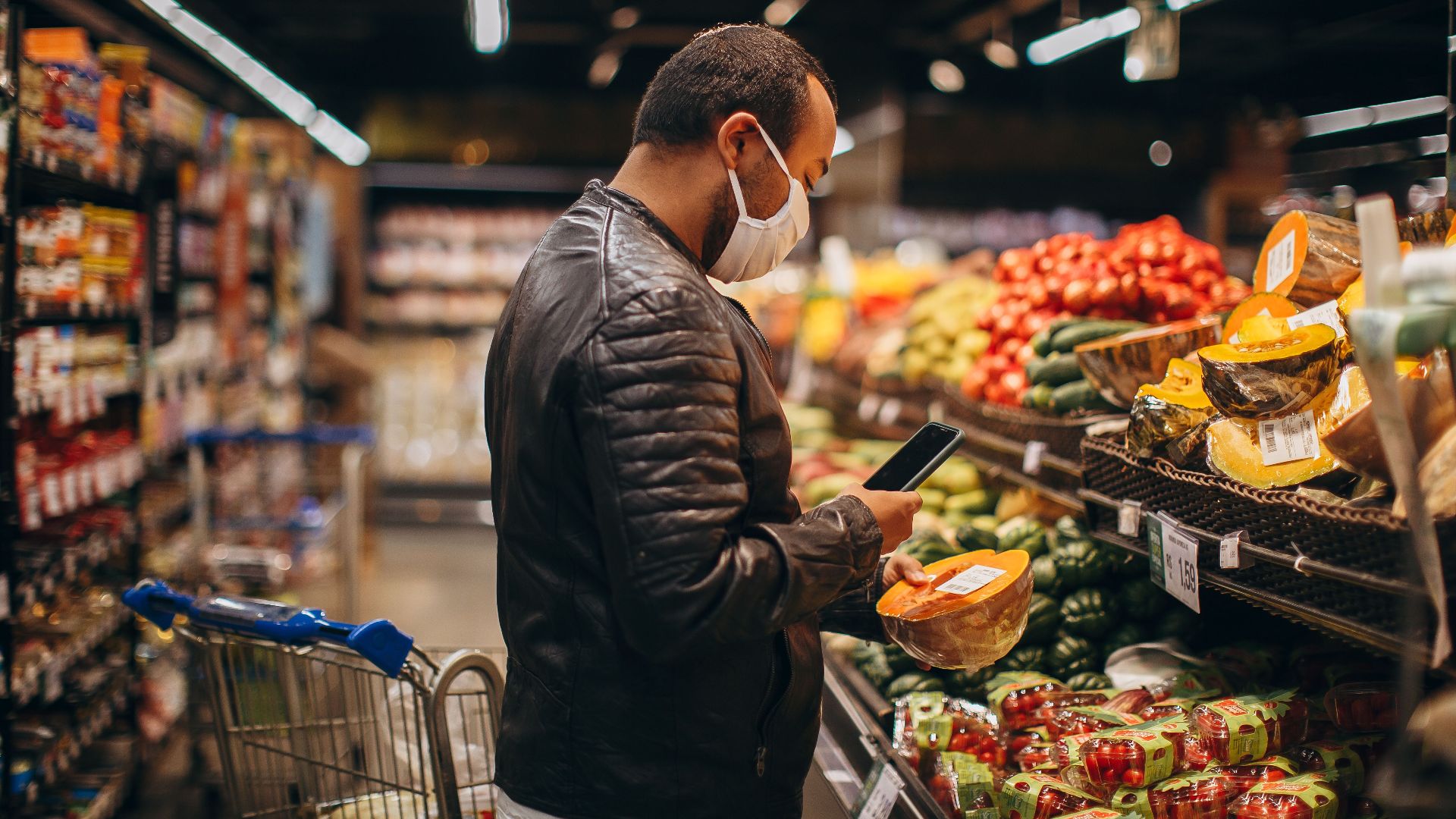 Man shopping in grocery store, inspecting fresh produce while wearing a mask.