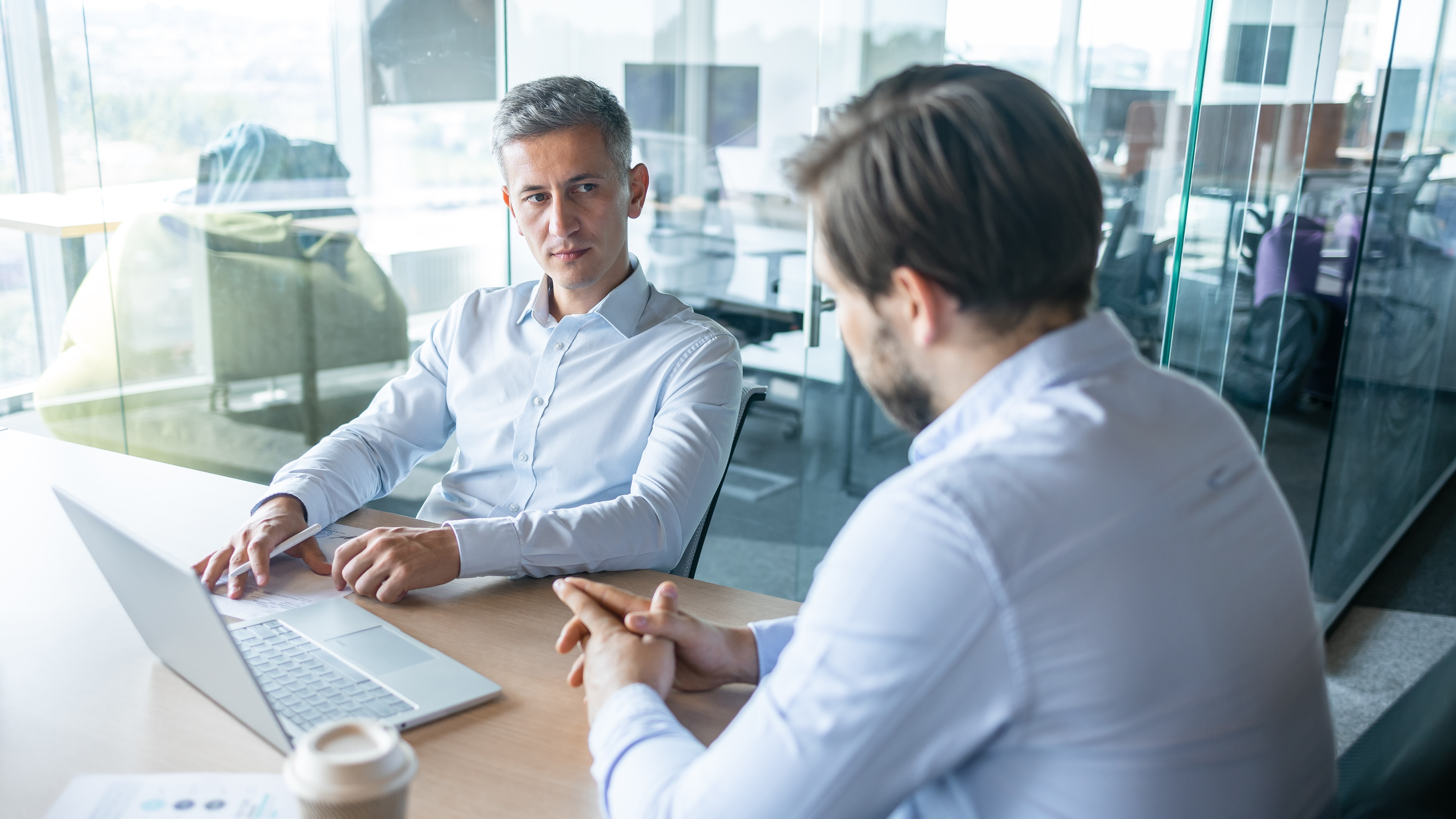 Two businessmen seated in a modern office, having serious discussion.