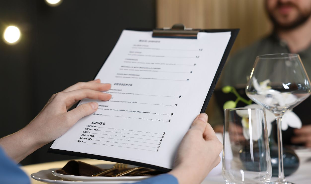 Couple choosing dishes from menu at table in restaurant, closeup