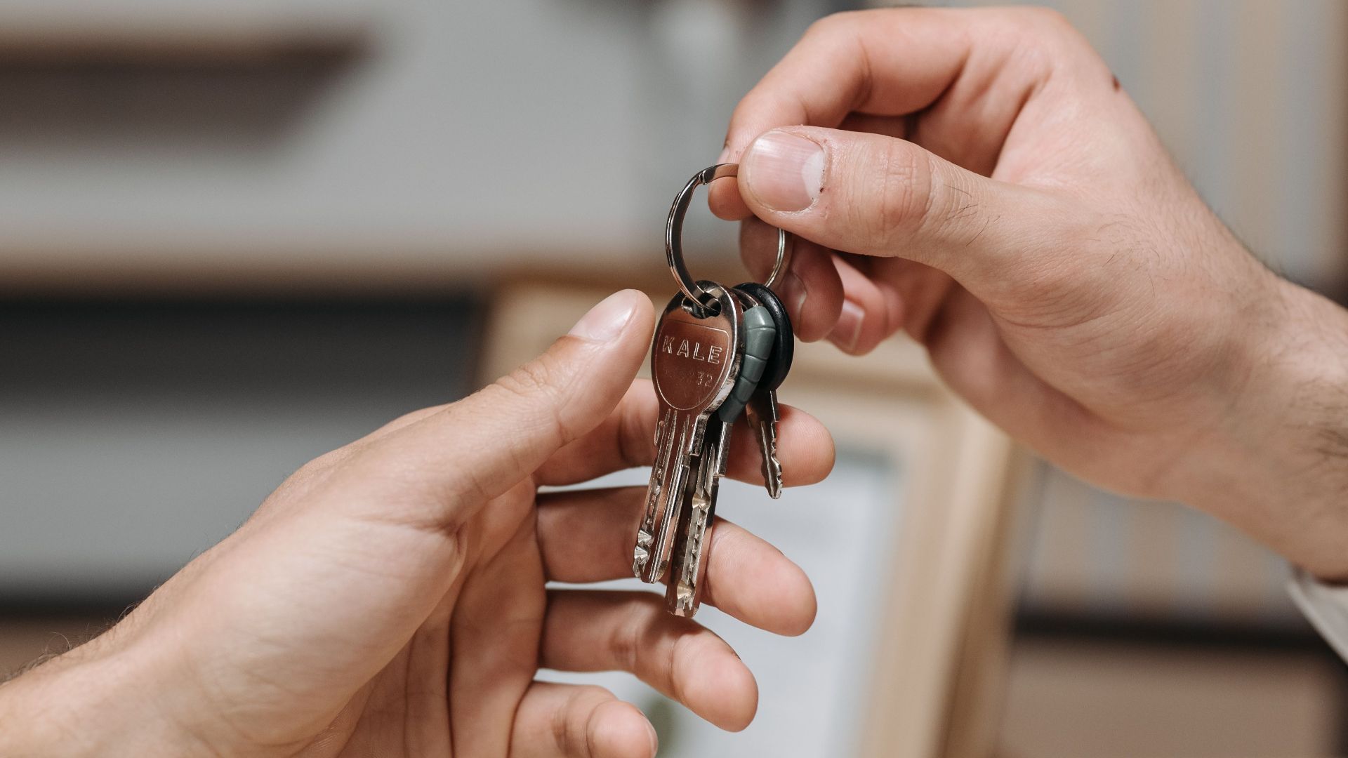 A close-up image of two hands exchanging a set of keys indoors.