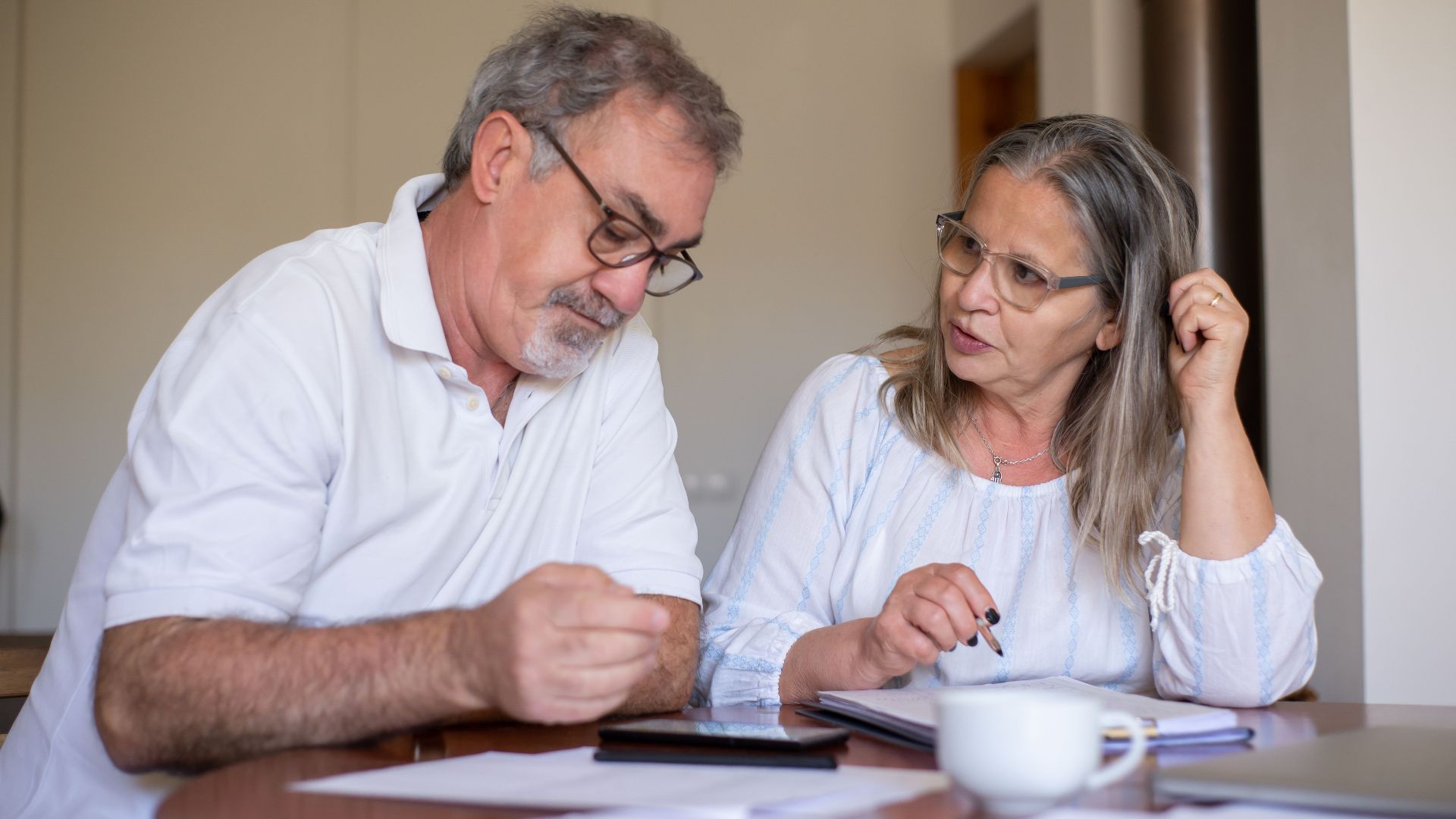 Senior couple reviewing documents and managing finances together at home, showing collaboration and care.