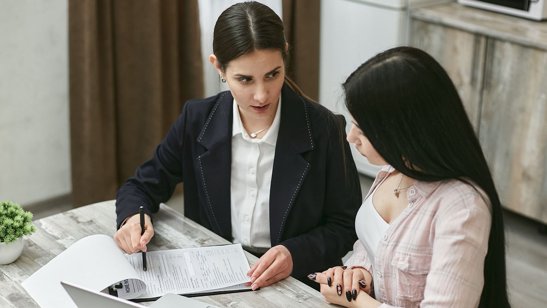 Two businesswomen engaged in a contract discussion at an office table.