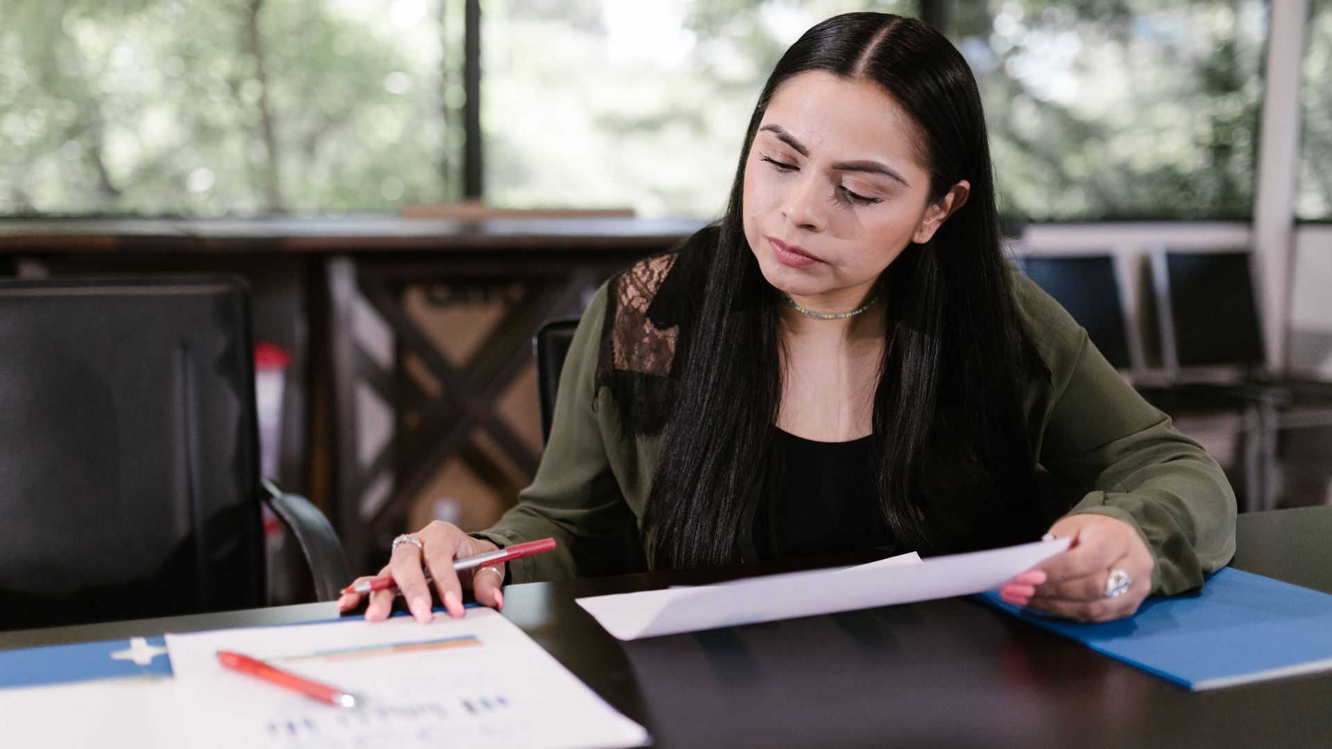 Professional woman in office setting studying documents with concentration.