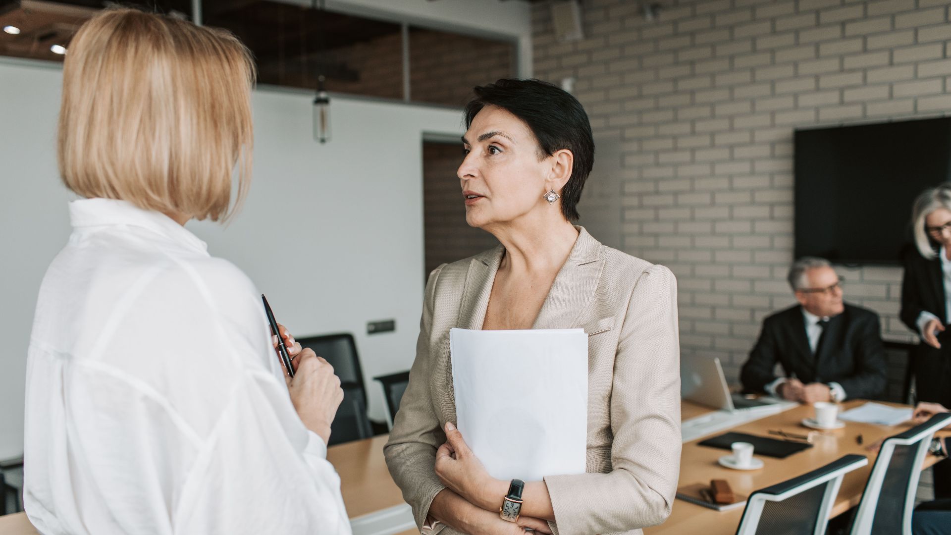 Two businesswomen engage in a conversation during a professional meeting in a modern office.