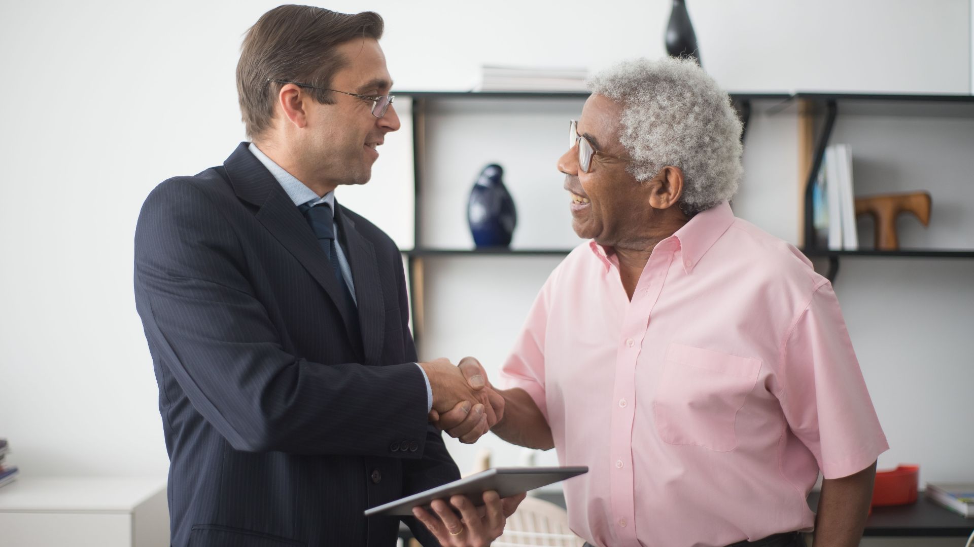 Two businessmen shaking hands during a meeting in a bright office environment.