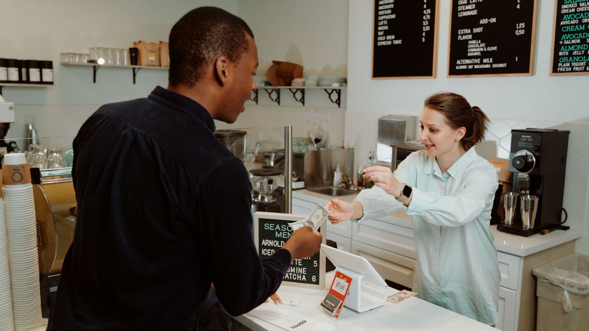 A customer pays for coffee at a café counter, transaction with barista.