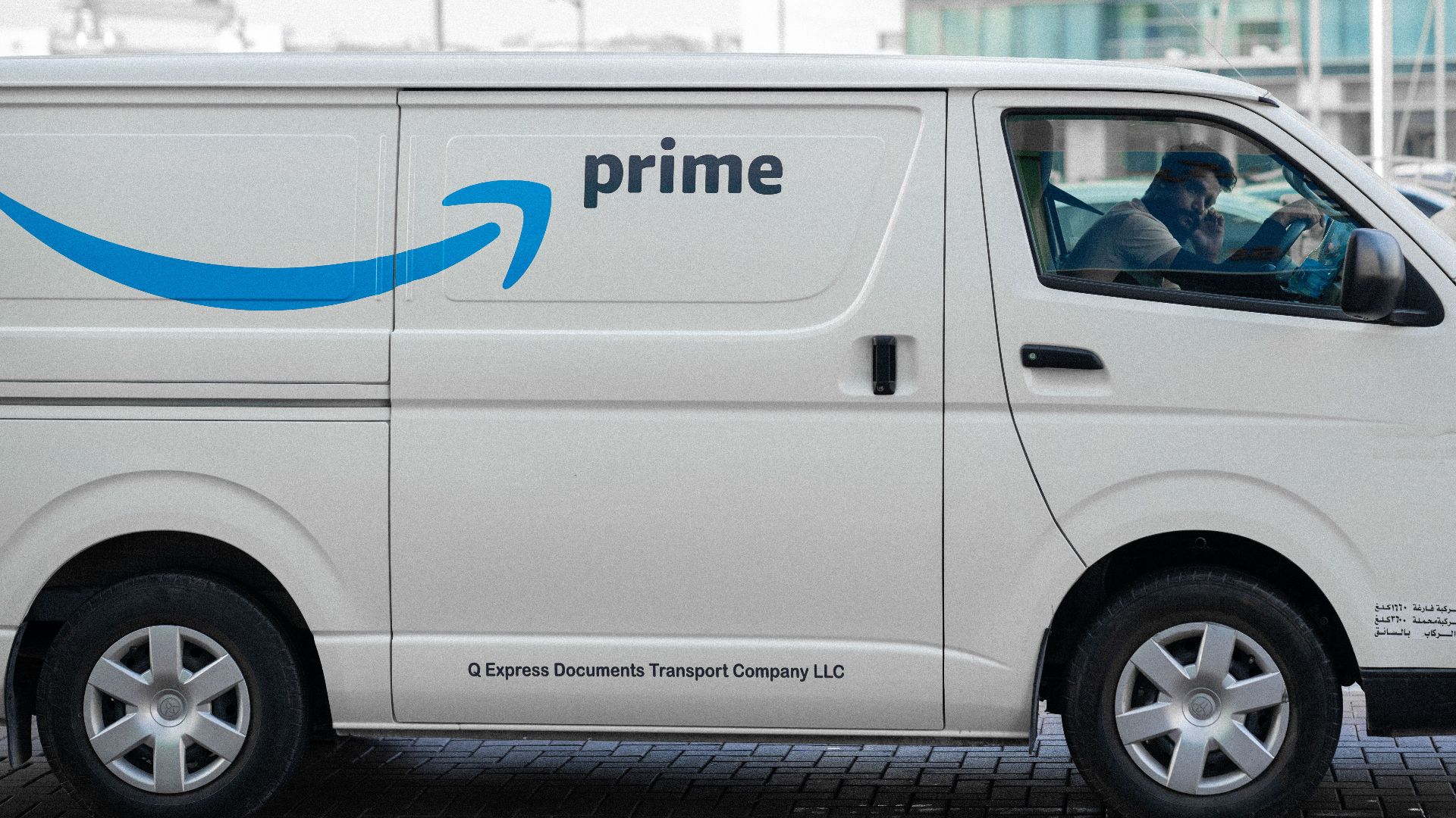 A white delivery van with Prime logo parked on an urban street with driver inside.