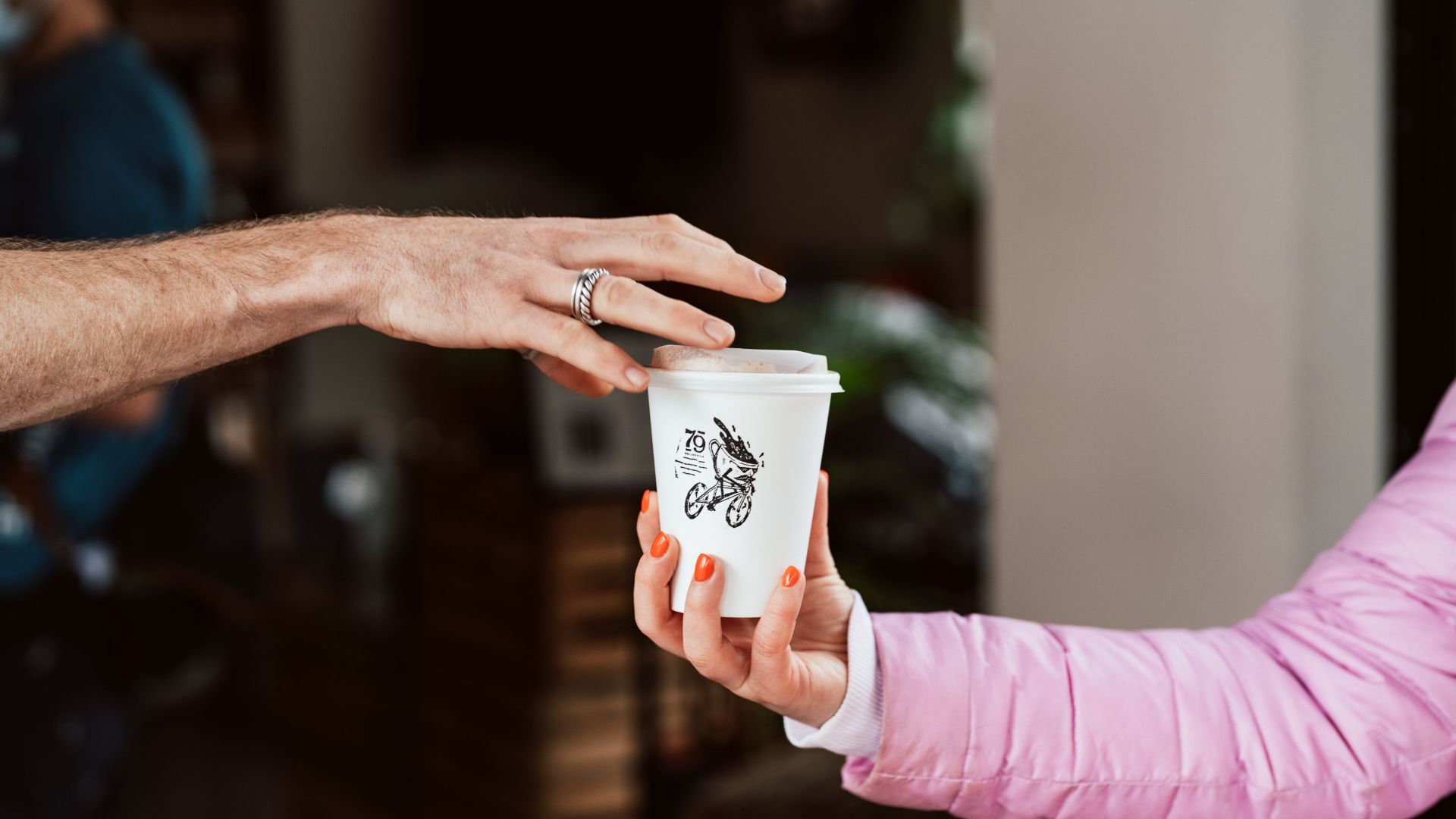 Two people exchanging a takeaway cup in a London cafe, showcasing warm interaction.
