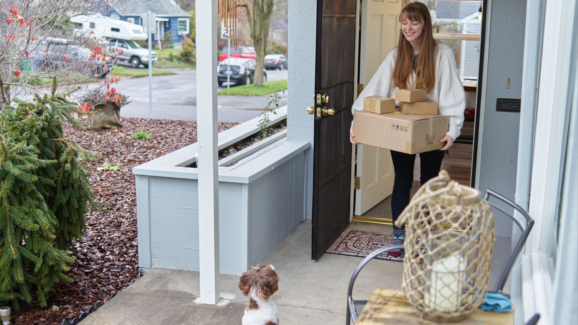 Smiling woman receives packages at her door, watched by a small dog.