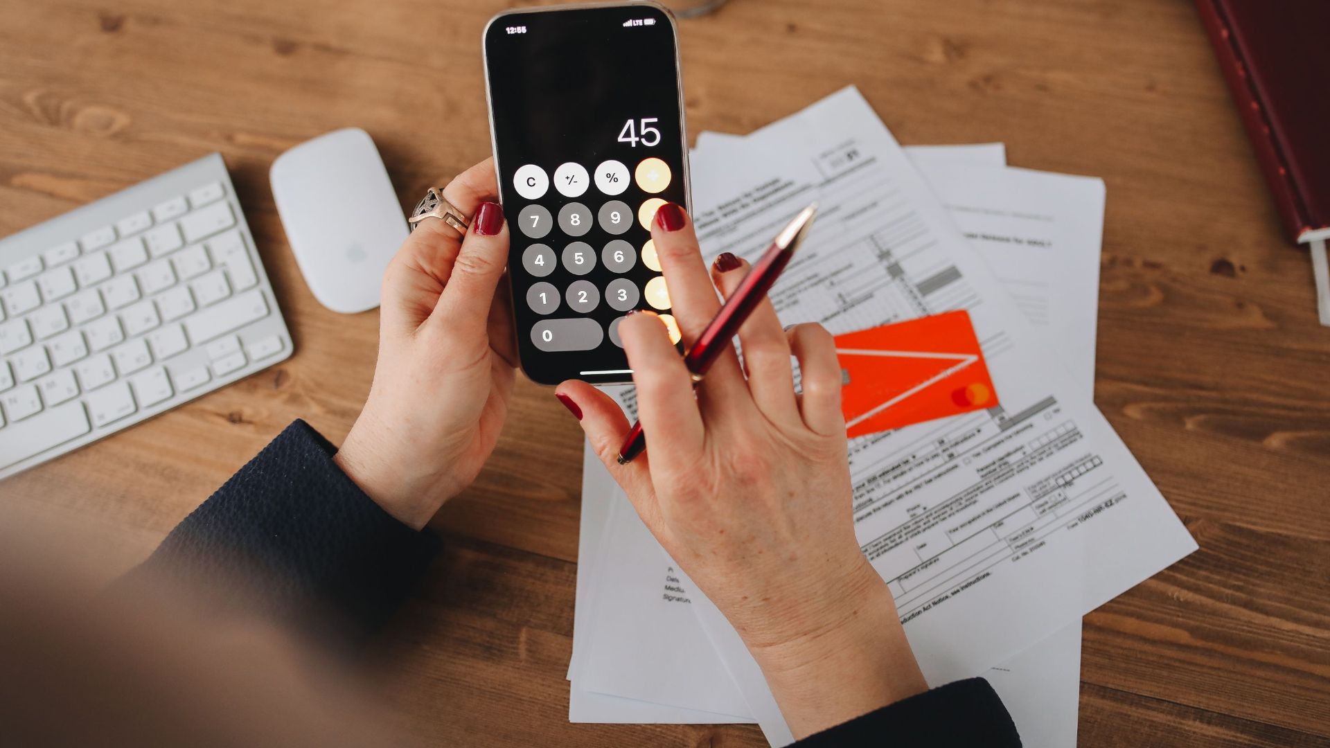 Hands using a calculator app on a smartphone over financial documents. Perfect for illustrating finance or technology themes.