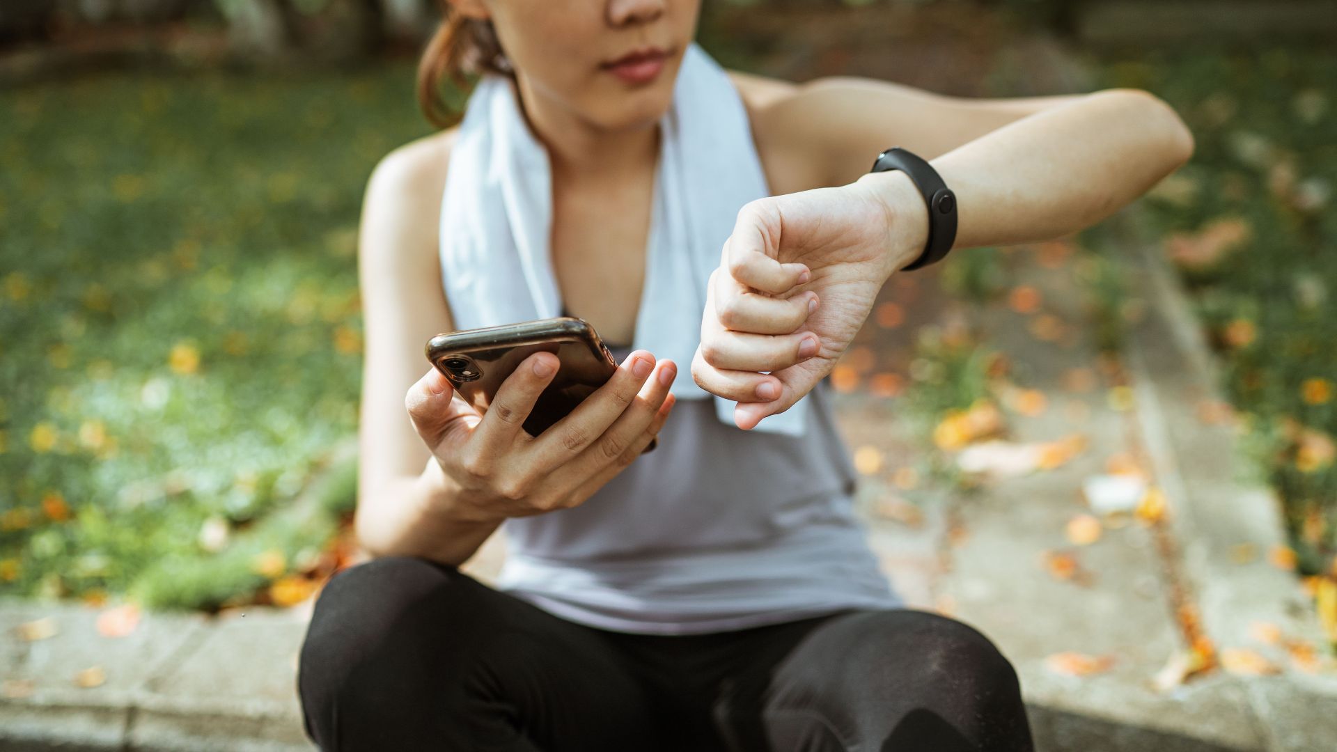 Anonymous female in sportswear using smartphone and smart watch after exercising on sports ground