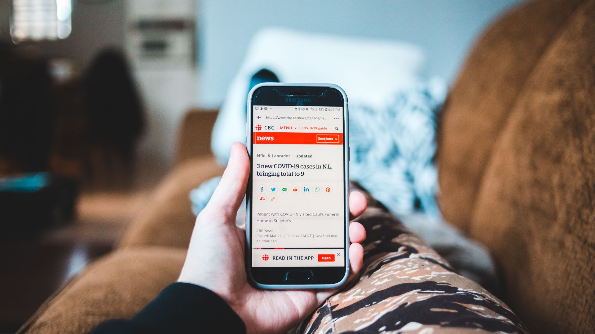 A person browsing news on a smartphone while relaxing on a sofa indoors.