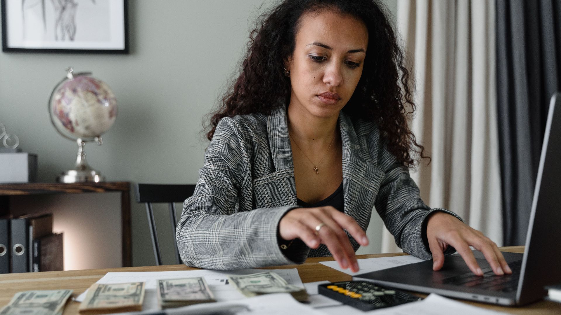 Professional woman analyzing financial documents and counting cash at office desk.