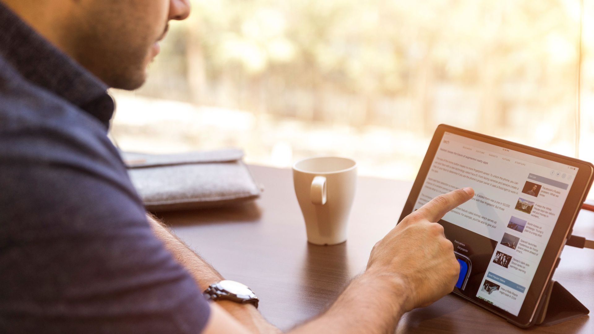 Adult man browsing a tablet with coffee indoors during the day.