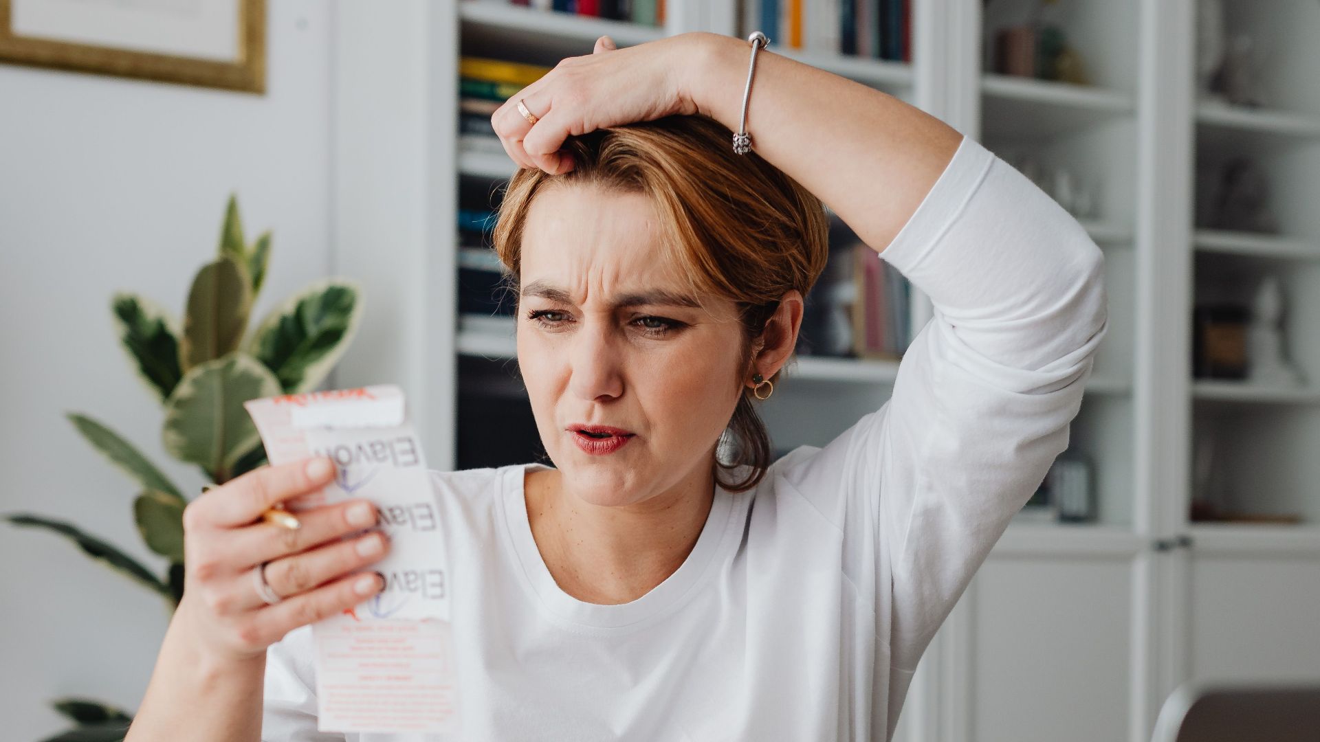 Woman sitting at desk looking stressed while reviewing receipts, depicting financial concern