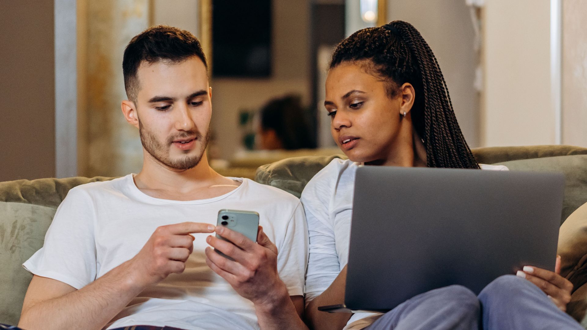 A couple sitting together on a couch, using a laptop and smartphone, enjoying a cozy moment.