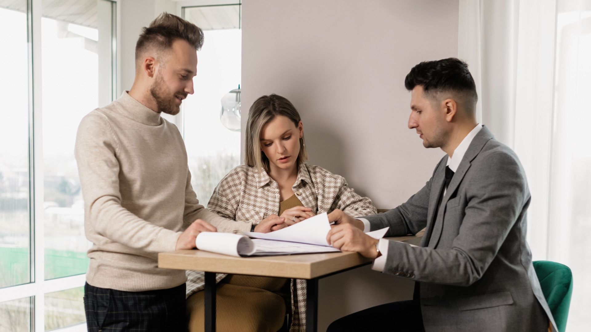 Pregnant couple reviewing property documents with a real estate agent in a bright modern interior.