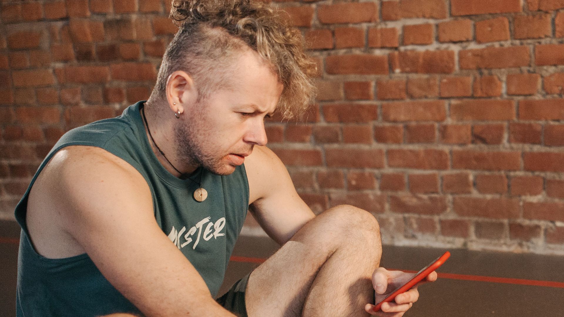 Man sitting on exercise mat using laptop and smartphone indoors.