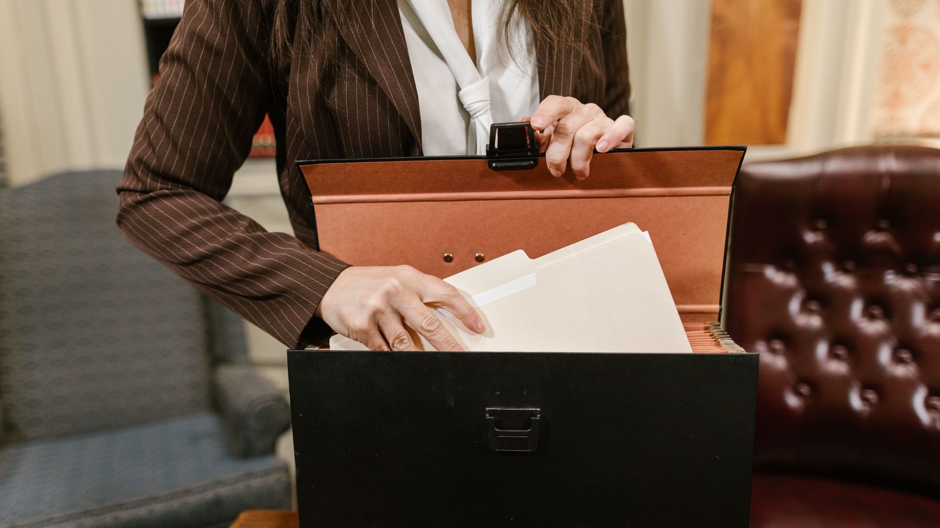 Close-up of a businesswoman organizing files in a black box in an office setting.