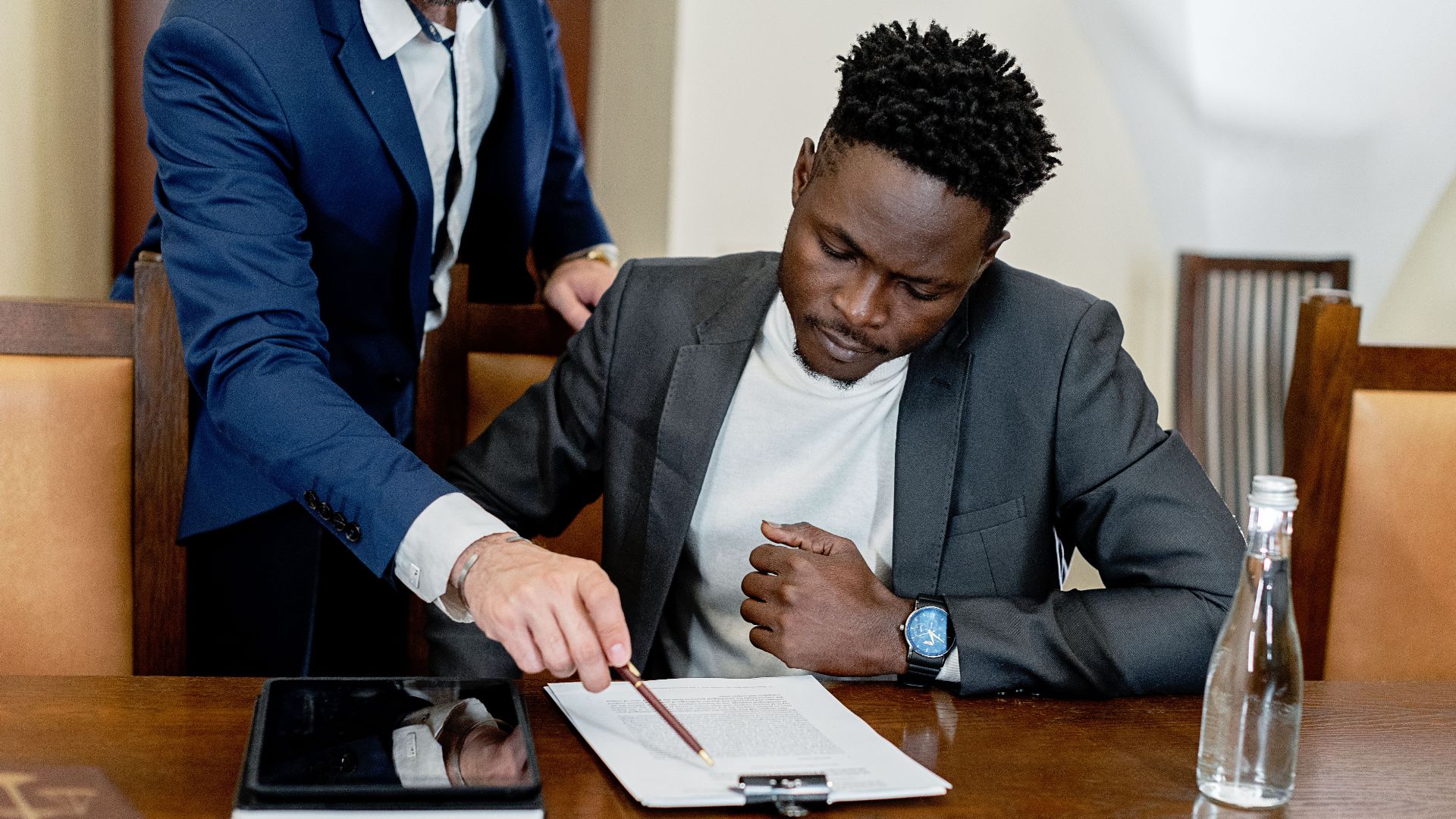 Two businessmen in a legal consultation reviewing a document with a tablet on the desk.