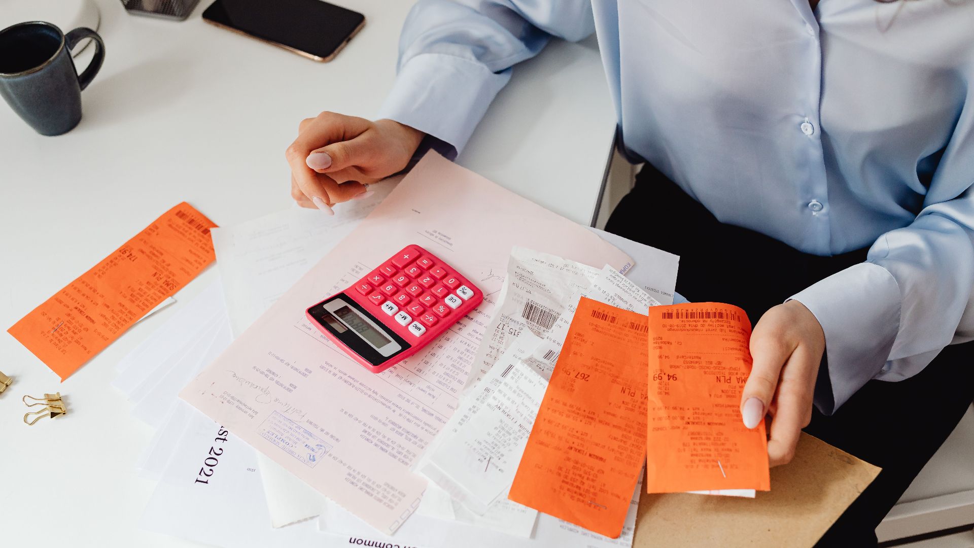 A woman reviews receipts and calculates expenses at a desk with a pink calculator.