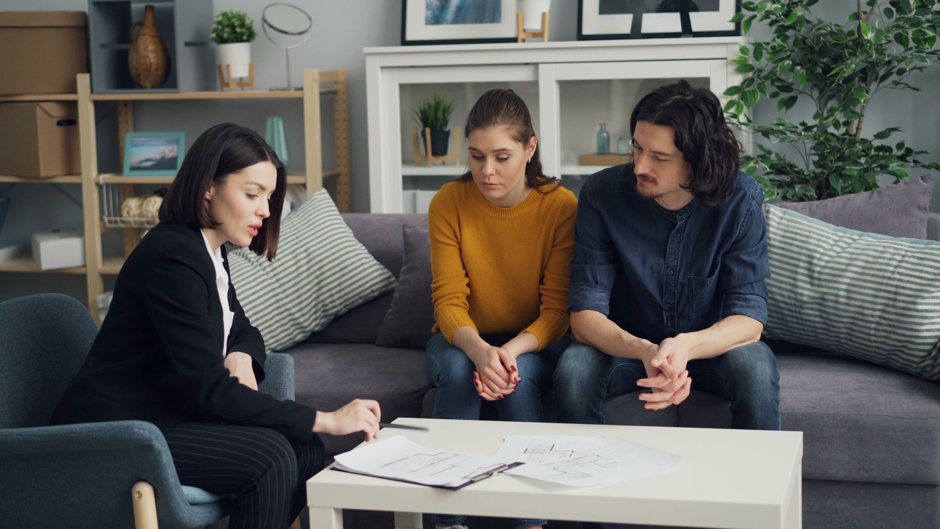 Couple discussing property with real estate agent in cozy living room setting, reviewing documents.