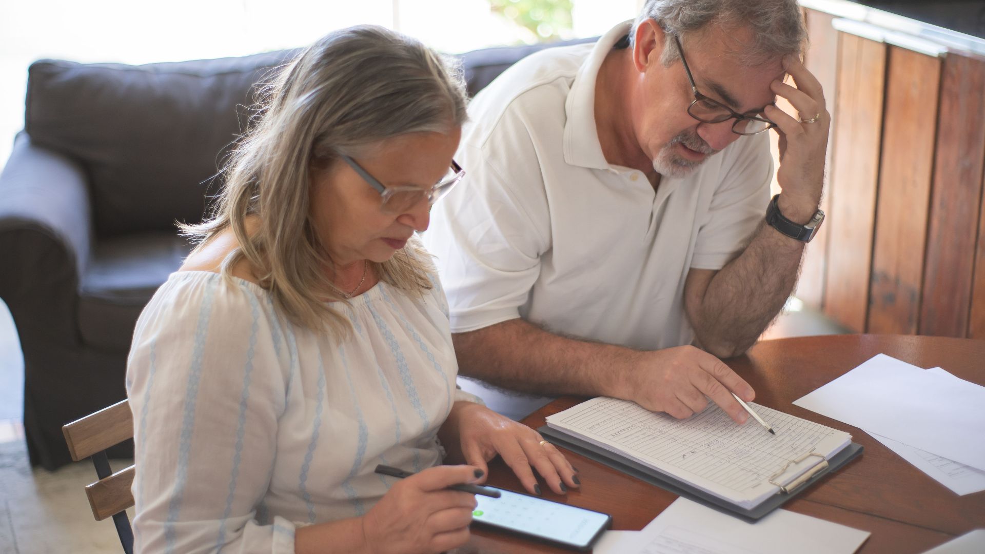 Elderly couple reviewing bills and documents at home, focusing on finances and technology.