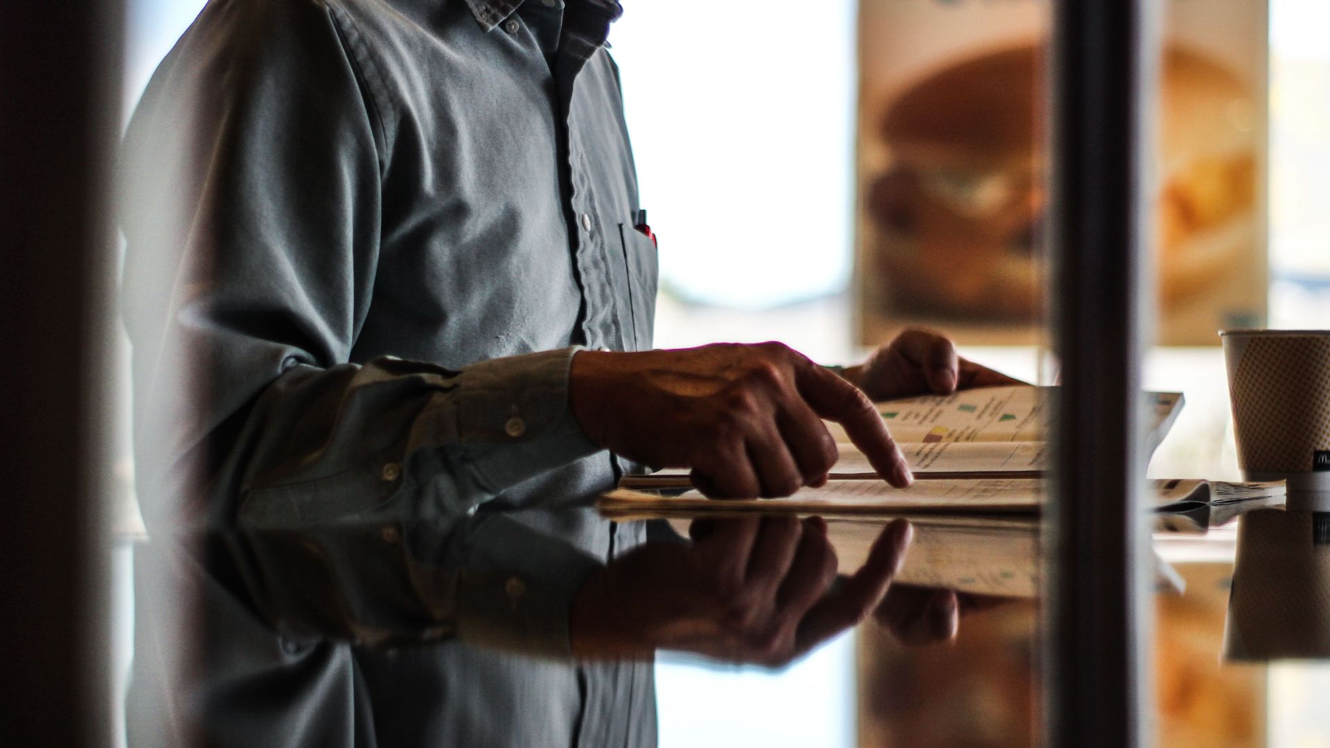 An adult man reads a newspaper indoors at a cafe, reflecting thoughtfully.