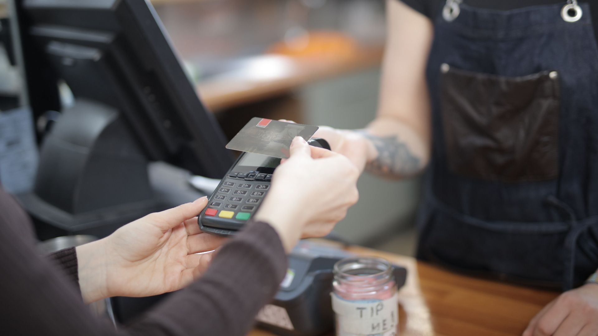 Close-up of customer and cashier during a credit card transaction at a store counter indoors.