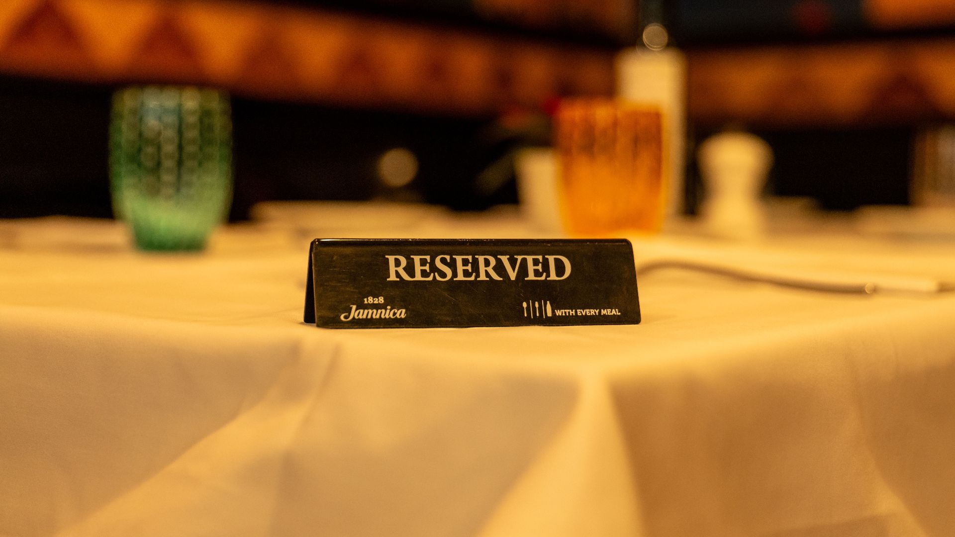 Close-up of a reserved sign on a white tablecloth in a dimly lit restaurant setting.